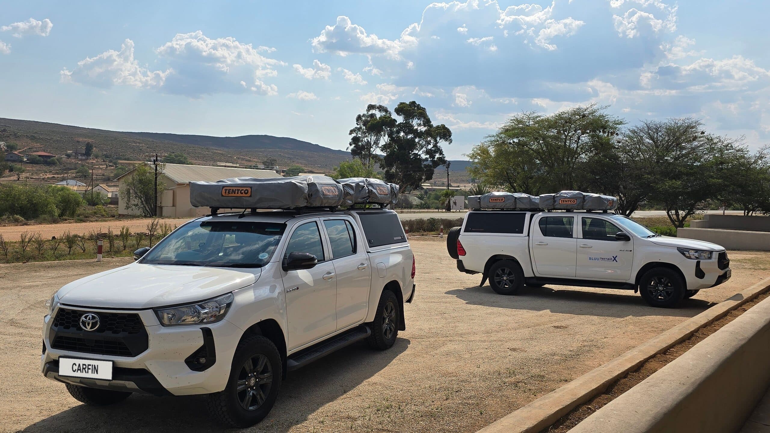 Two white Toyota Hilux double cabs parked on a gravel yard